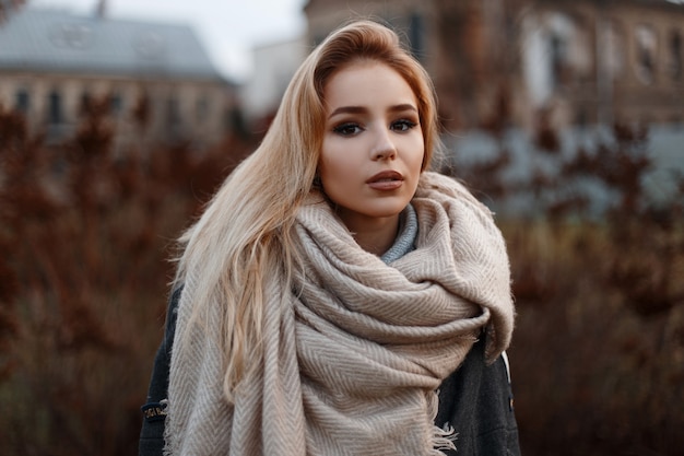 Ritratto di una bella ragazza giovane attraente in un elegante cappotto nero con una sciarpa vintage beige in guanti neri in un maglione lavorato a maglia