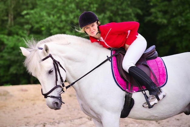 Ritratto di una bella ragazza giovane donna cavaliere equestre su cavallo bianco in casco e polo shirt