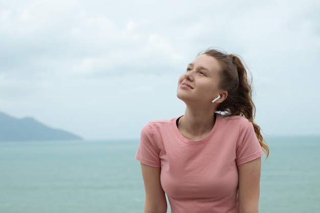 Ritratto di una bella ragazza in auricolari sullo sfondo naturale dell'oceano o del mare in montagna