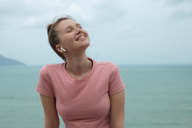 Ritratto di una bella ragazza in cuffia sullo sfondo naturale dell'oceano o del mare in montagna giovane donna sorride ascolta musica e si rilassa all'aria aperta e respira profondamente durante il giorno d'estate