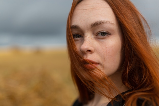 Ritratto di una bella ragazza sensuale con lunghi capelli rossi che si trova nella natura e guarda direttamente nella telecamera. Foto di alta qualità