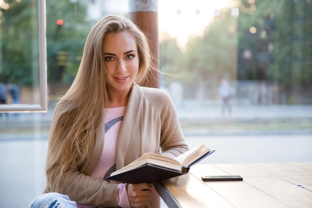 Ritratto di una bella ragazza sorridente seduta con un libro al bar