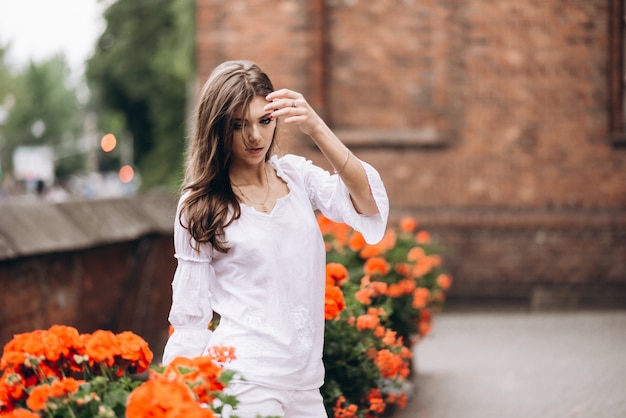 Ritratto di una bella ragazza vestita di bianco e in piedi vicino ai fiori