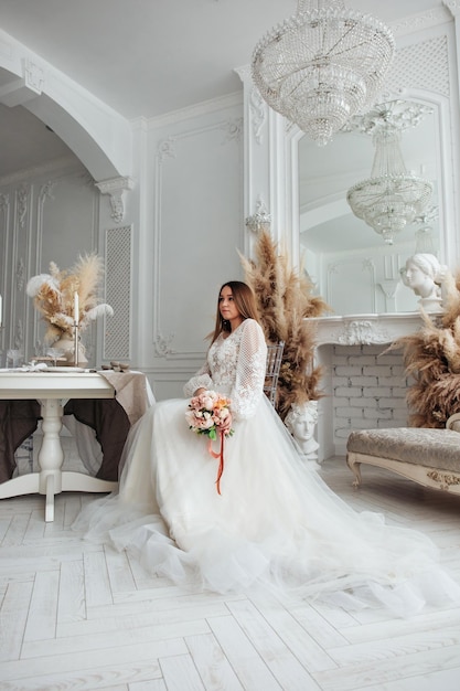 Ritratto di una bella sposa con un bouquet di ortensie arancio pastello e rose in mano in un interno chiaro