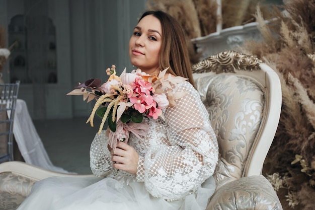 Ritratto di una bella sposa con un bouquet di rose di ortensie e feci in colore arancione pastello nelle sue mani in un interno chiaro