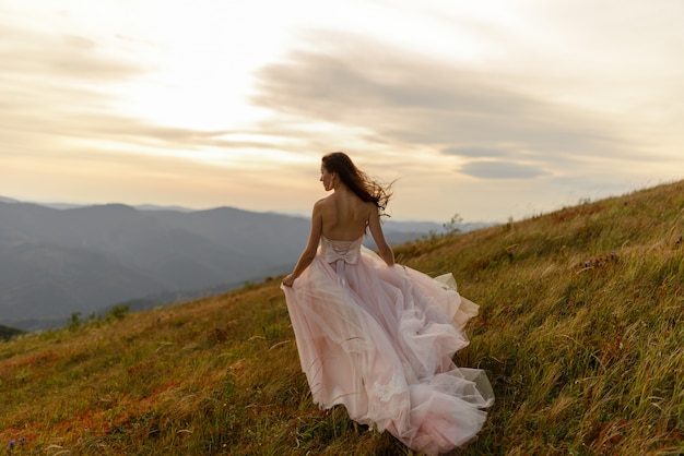 Ritratto di una bella sposa su un paesaggio di montagne autunnali. Un forte vento le soffia i capelli e il vestito. Cerimonia di nozze in cima alla montagna.