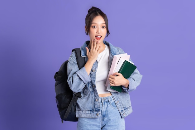 Ritratto di una bella studentessa asiatica che indossa uno zaino su uno sfondo viola