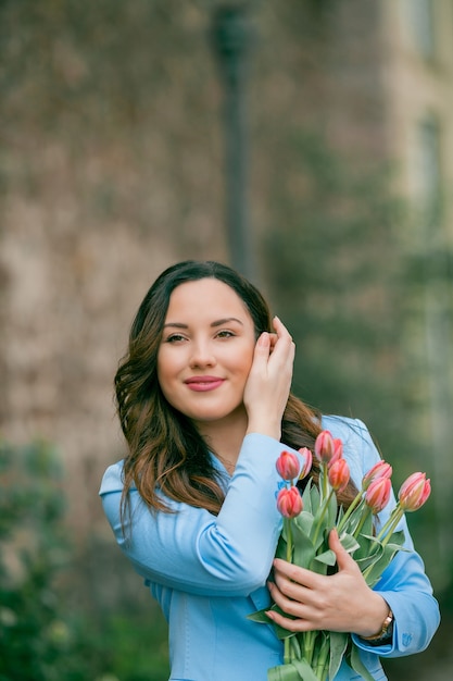 Ritratto di una bellissima giovane donna in abito blu con un mazzo di tulipani