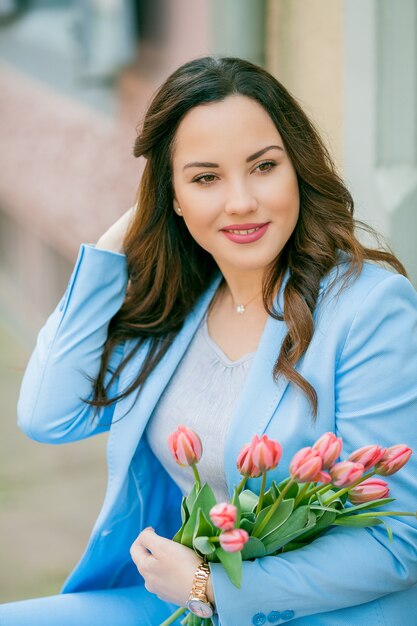 Ritratto di una bellissima giovane donna in abito blu con un mazzo di tulipani