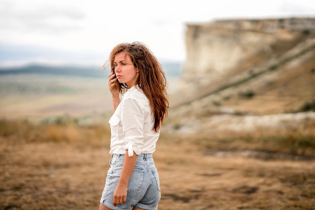 Ritratto di una bellissima giovane donna in camicia bianca sul bordo di una scogliera con panorama infinito