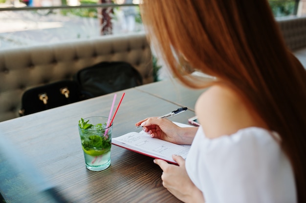 Ritratto di una bellissima giovane imprenditrice di successo scrivendo qualcosa nel suo quaderno rosso mentre era seduto in un caffè.