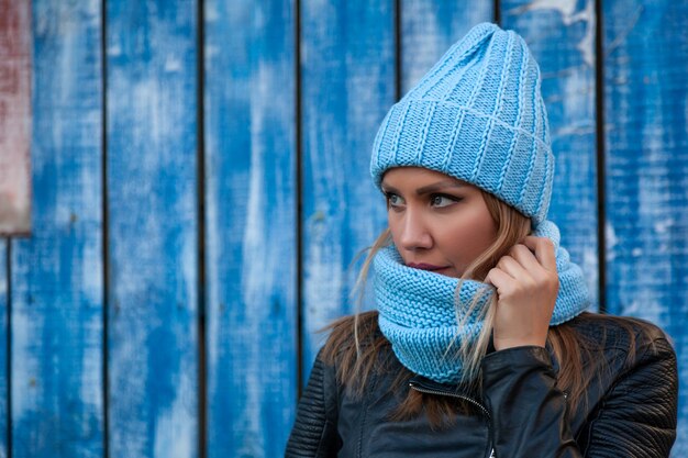 Ritratto di una bellissima giovane modella con un cappello a maglia blu in piedi vicino al muro blu in una giornata autunnale