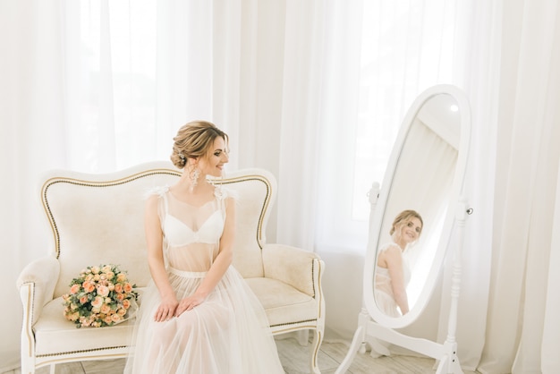 Ritratto di una bellissima giovane sposa in una stanza luminosa in un'atmosfera romantica. Sposa in vestaglia con un mazzo di nozze