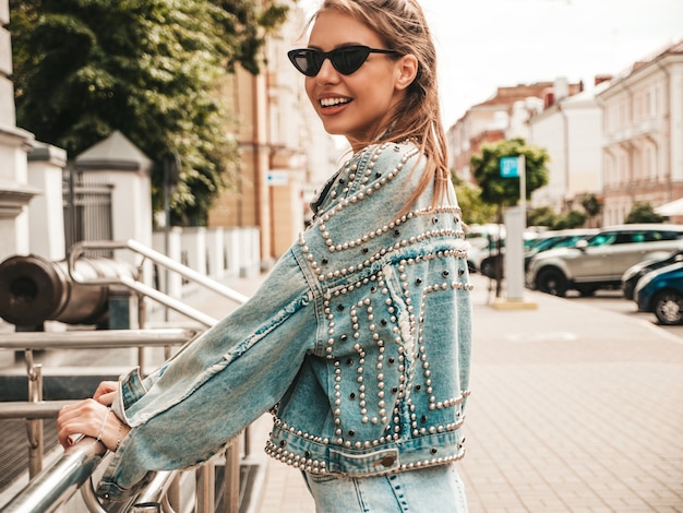 Ritratto di una bellissima modella sorridente vestita con una giacca di jeans hipster estiva