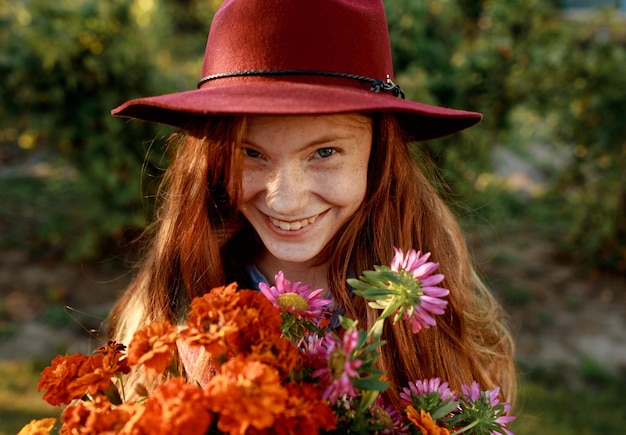 Ritratto di una bellissima ragazza dai capelli rossi con un cappello rosso che tiene in mano un mazzo di fiori