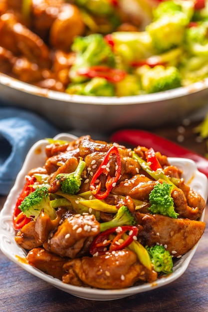 Ritratto di una ciotola di pollo teriyaki cosparsa di semi di sesamo, peperoncini freschi e broccoli con più cibo in una ciotola nella parte posteriore.