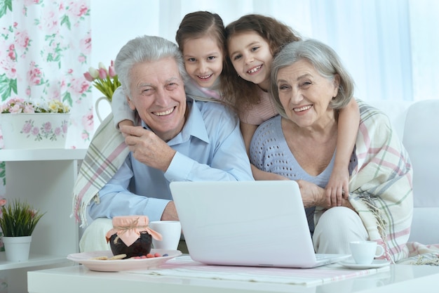 Ritratto di una coppia anziana felice con nipoti e laptop a casa
