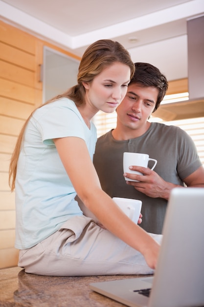 Ritratto di una coppia che mangia caffè mentre usando un computer portatile