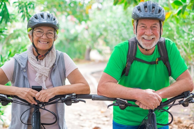 Ritratto di una coppia di anziani vecchi e felici innamorati che guardano la telecamera sorridendo e divertendosi con le loro biciclette in natura all'aperto insieme sentendosi bene e in salute