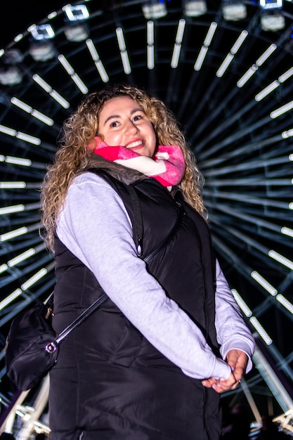 Ritratto di una donna ad una fiera con una ruota panoramica sorridente che guarda l'obbiettivo di notte