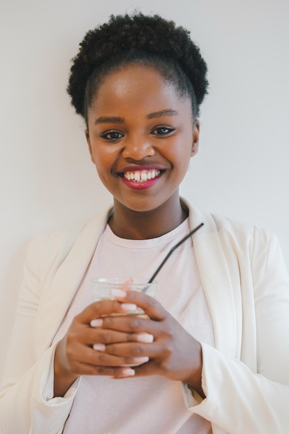 Ritratto di una donna afroamericana sorridente tenendo un bicchiere guardando la fotocamera isolata su muro bianco Bella ragazza ritratto Bella donna nera