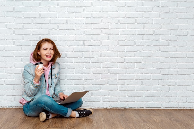 Ritratto di una donna allegra che si siede sul pavimento con il computer portatile