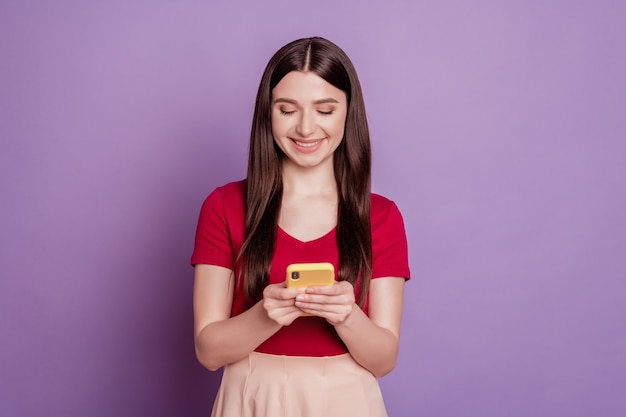 Ritratto di una donna allegra e adorabile che tiene lo schermo dello smartphone con un sorriso raggiante su sfondo viola