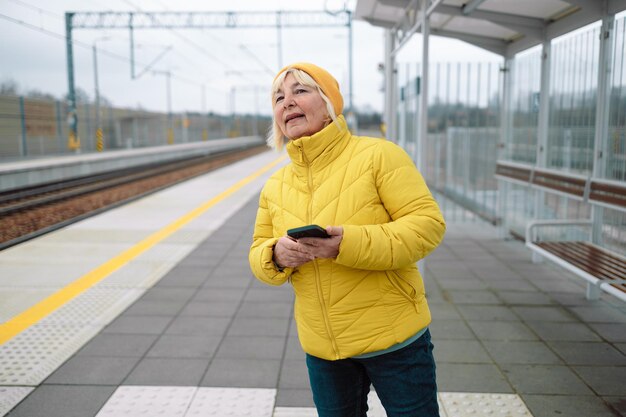 Ritratto di una donna anziana che usa il telefono cellulare mentre aspetta alla stazione del tram foto di alta qualità