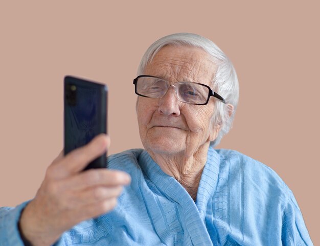 Ritratto di una donna anziana di 90 anni che indossa occhiali e giacca blu che tiene in mano la telecamera e si fa un selfie