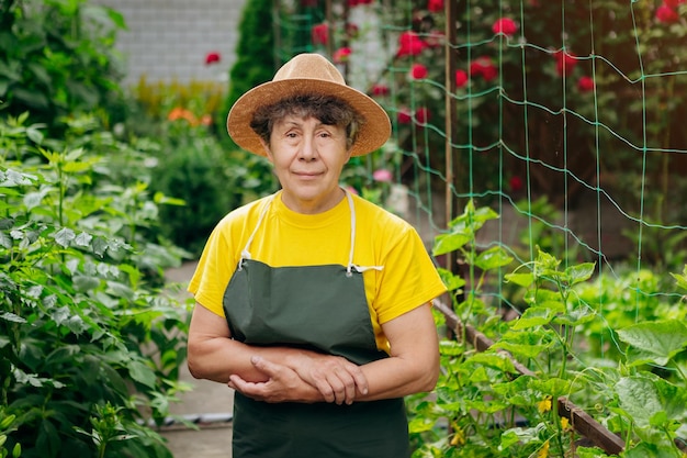 Ritratto di una donna anziana giardiniere in un cappello che lavora nel suo cortile Il concetto di giardinaggio che cresce e si prende cura di fiori e piante