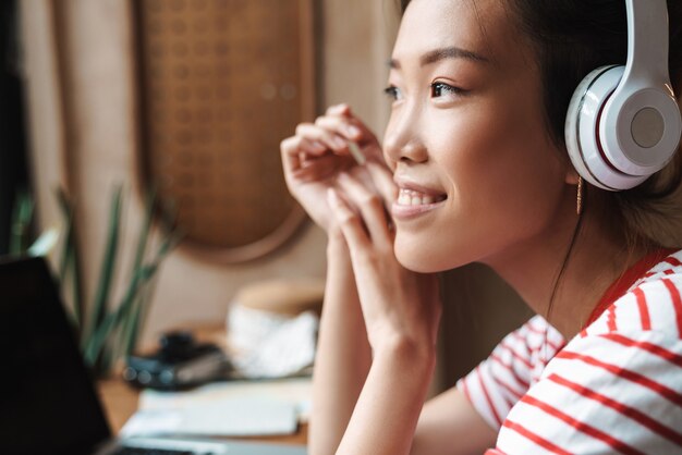 Ritratto di una donna asiatica adorabile che ascolta musica con le cuffie mentre è seduta al bar al chiuso