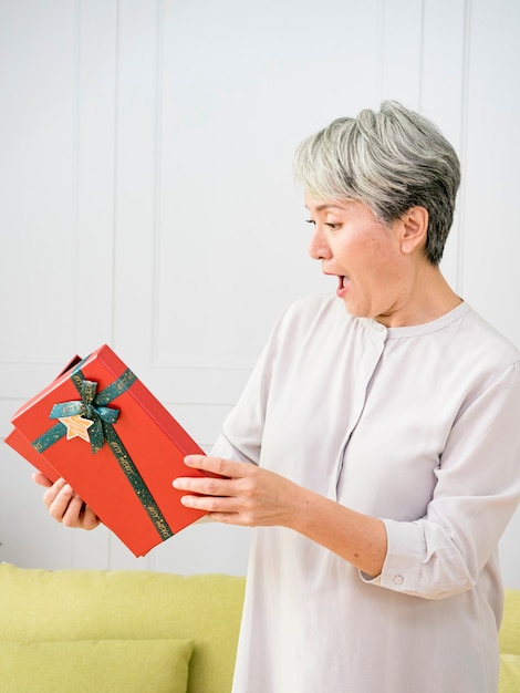 ritratto di una donna asiatica anziana che tiene in mano una confezione regalo, sorpresa a casa.