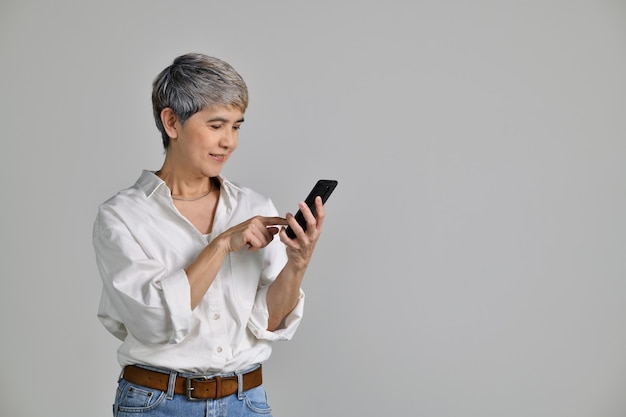 Ritratto di una donna asiatica di mezza età allegra che punta il dito su uno smartphone isolato su sfondo bianco