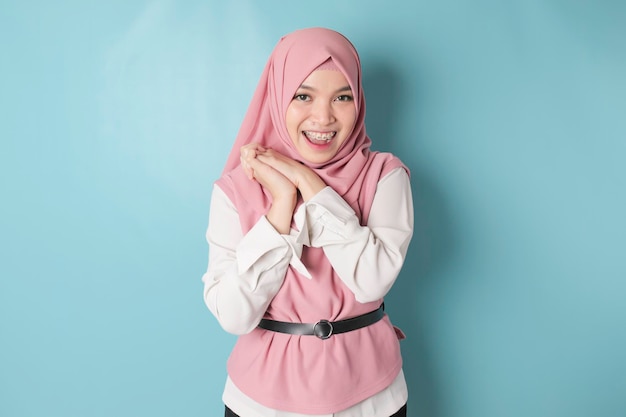 Ritratto di una donna asiatica musulmana allegra in piedi e sorridente alla telecamera isolata su sfondo blu