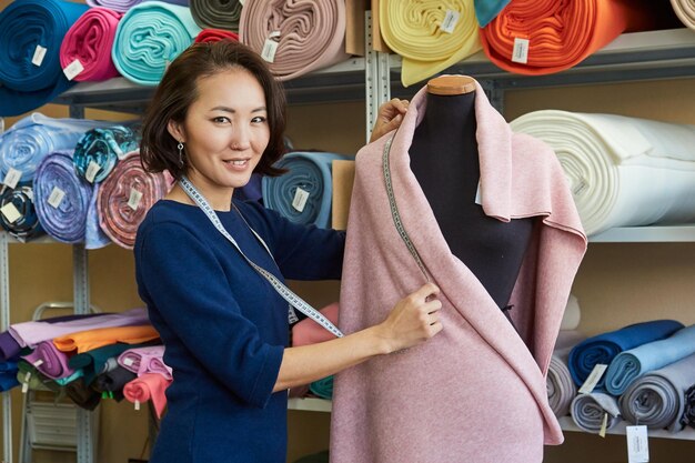 Ritratto di una donna asiatica sorridente di affari che prende le misure su un manichino nella sua officina