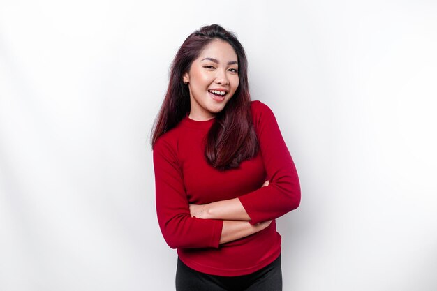 Ritratto di una donna asiatica sorridente fiduciosa vestita di rosso in piedi con le braccia conserte e guardando la telecamera isolata su sfondo bianco