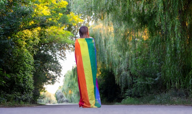 Ritratto di una donna attraente che tiene una bandiera gay arcobaleno LGBT sulle spalle, guardando al lato.