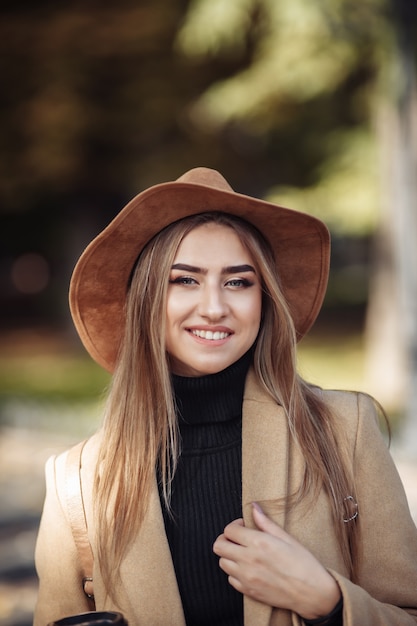 Ritratto di una donna attraente con trucco vestito con un cappotto e un cappello di feltro.