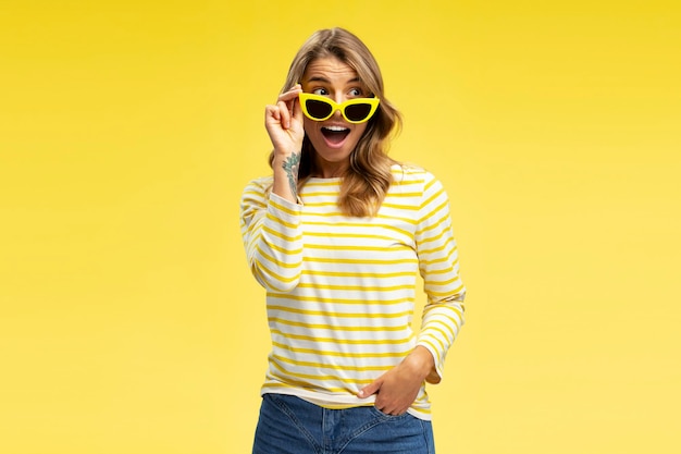 Ritratto di una donna attraente, eccitata e positiva che indossa eleganti occhiali da sole gialli che guarda altrove