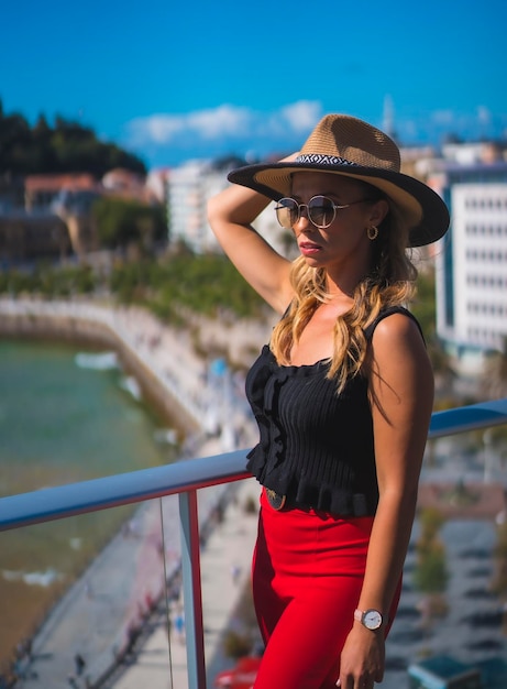 Ritratto di una donna bionda che trascorre le vacanze in un hotel di lusso su una terrazza con indosso un cappello