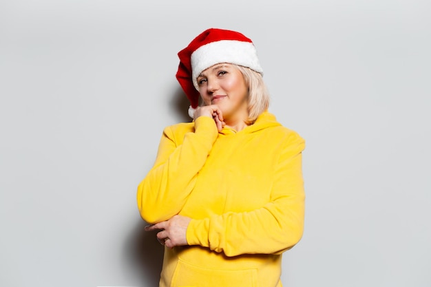 Ritratto di una donna bionda sorridente che indossa una felpa con cappuccio gialla con cappello di Natale