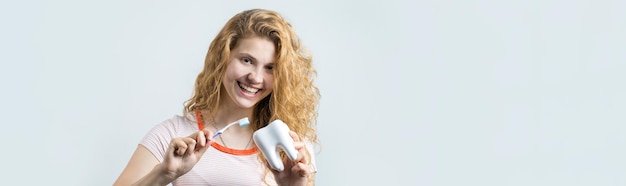 Ritratto di una donna carina sorridente con capelli ricci rossi che tiene lo spazzolino da denti isolato su uno sfondo bianco