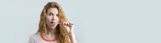 Ritratto di una donna carina sorridente con capelli ricci rossi che tiene lo spazzolino da denti isolato su uno sfondo bianco