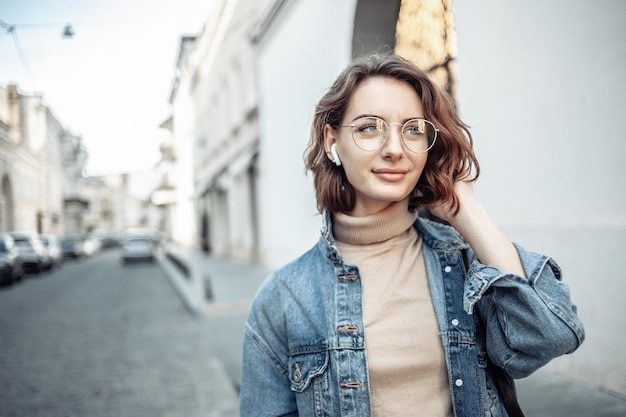 Ritratto di una donna carismatica, elegante e moderna, in abiti alla moda con occhiali e cuffie Attraente giovane donna che cammina lungo la strada urbana