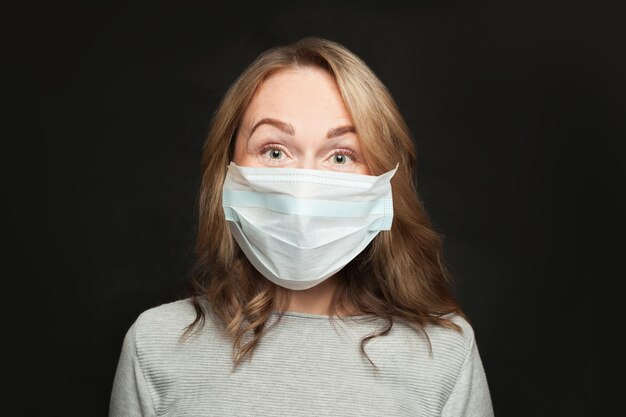 Ritratto di una donna casuale con una maschera protettiva medica su sfondo nero