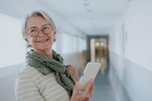 Ritratto di una donna caucasica anziana che cammina lungo un corridoio all'interno di un edificio che tiene il telefono cellulare