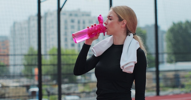 Ritratto di una donna che beve acqua dalla bottiglia sportiva rosa Ragazza in forma bere acqua dalla bottiglia Riposo dopo un duro treno di basket Attività sportive