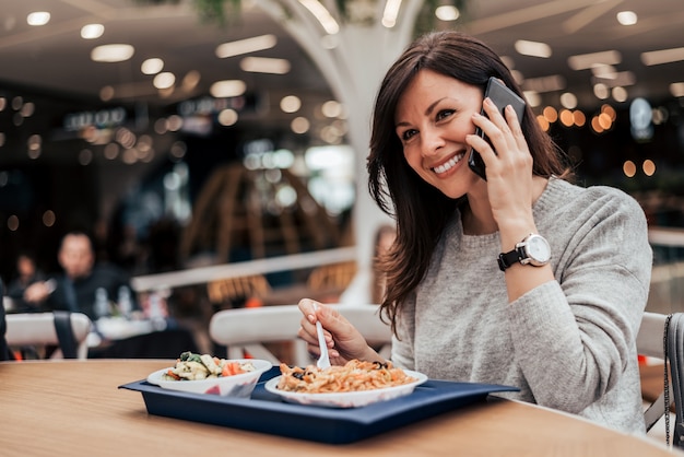 Ritratto di una donna che mangia nel ristorante fast food e parlando sul cellulare.
