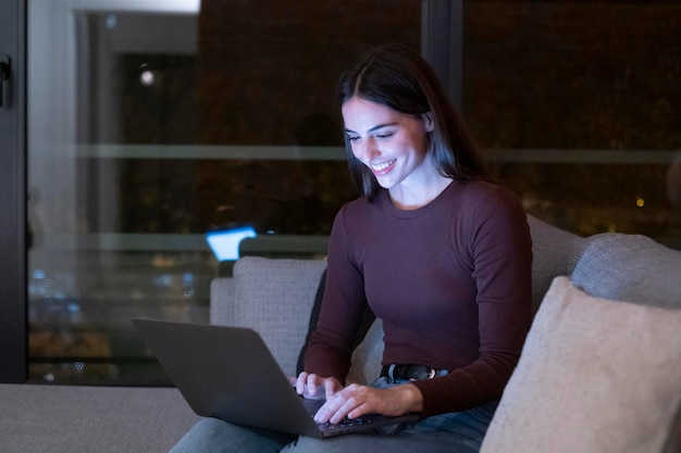 Ritratto di una donna che scrive sul portatile e sorride Attività ricreativa indoor felice Persone con computer Rilassarsi a casa seduti sul divano e chiacchierare sul notebook Persone con connessione online notturna