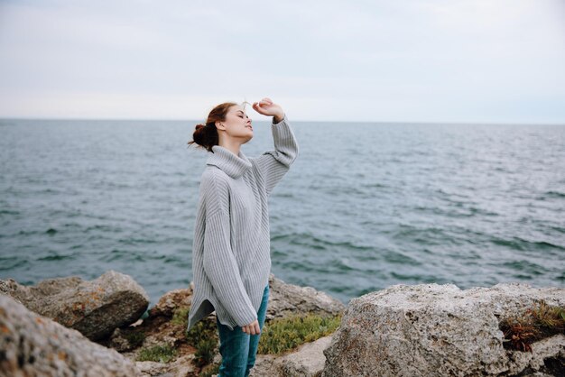 Ritratto di una donna con un maglione grigio in piedi su una riva rocciosa natura stile di vita foto di alta qualità
